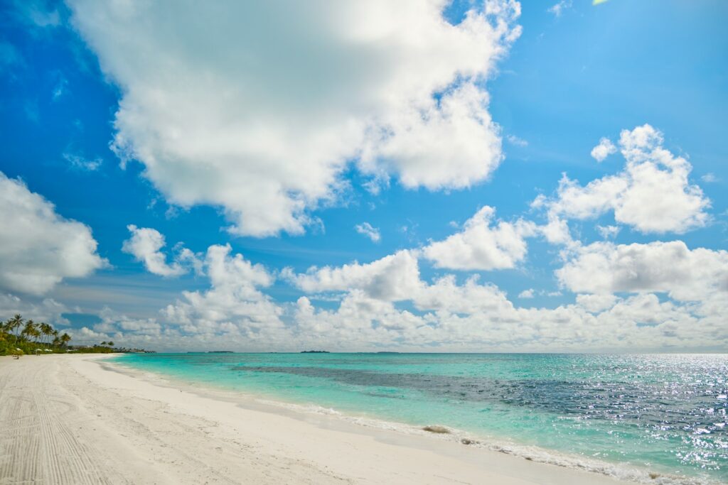 A sandy beach with clear blue water under a partly cloudy sky